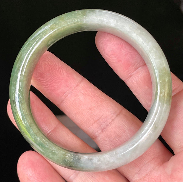 Close-up of fine crystalline texture and distinctive black accents on icy apple green and greyish white jadeite bangle