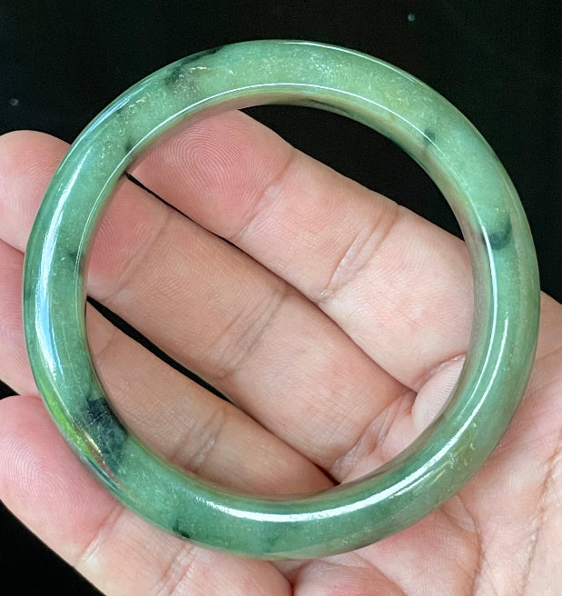 Close-up of fine crystalline texture and black floral inclusions on icy apple green jadeite bangle