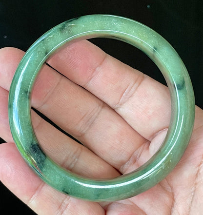Close-up of fine crystalline texture and black floral inclusions on icy apple green jadeite bangle