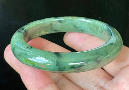 Close-up of fine crystalline texture and black floral inclusions on icy apple green jadeite bangle