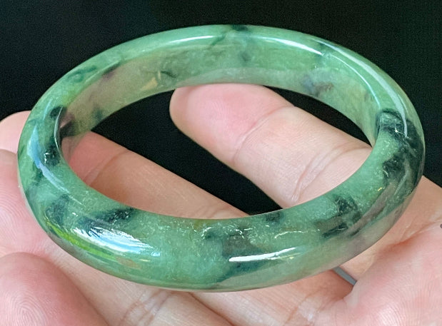 Close-up of fine crystalline texture and black floral inclusions on icy apple green jadeite bangle