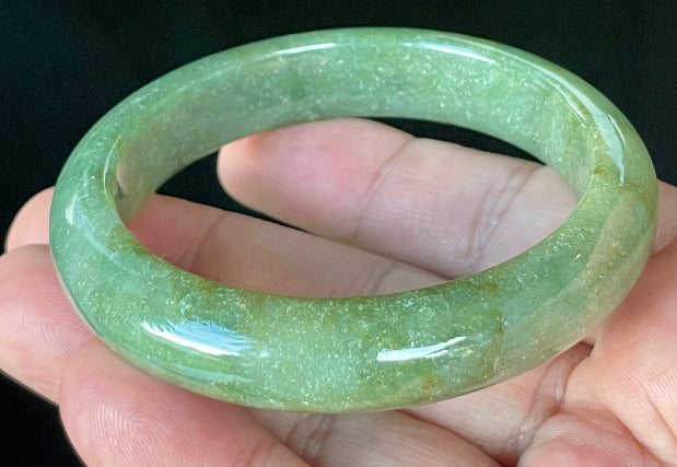 Close-up of fine crystalline texture and warm honey hues on icy apple green and white jadeite bangle