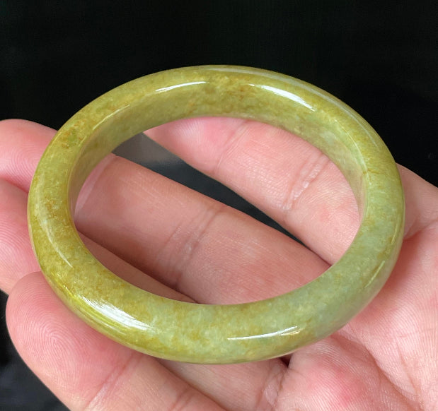 Close-up of fine crystalline texture and earthy brown undertones on moss and apple green jadeite bangle