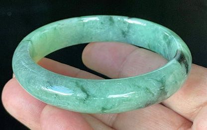 Close-up of fine crystalline texture and floral moss in the snow effect on icy apple green and black jadeite bangle