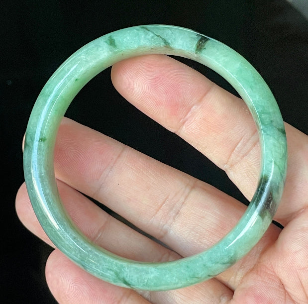 Close-up of fine crystalline texture and floral moss in the snow effect on icy apple green and black jadeite bangle