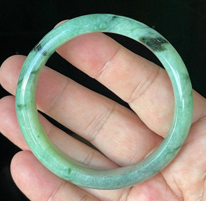Close-up of fine crystalline texture and floral moss in the snow effect on icy apple green and black jadeite bangle