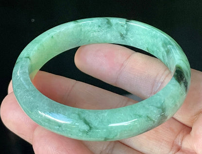 Close-up of fine crystalline texture and floral moss in the snow effect on icy apple green and black jadeite bangle
