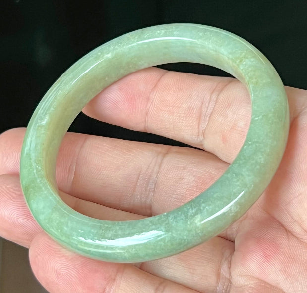 Close-up of fine crystalline texture and subtle cloud-like patterns on icy apple green jadeite bangle