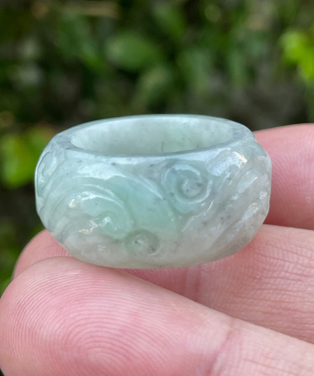 Close-up of graceful hand-carved swirl motif and fine crystalline texture on an icy bluish apple green Burmese jade ring