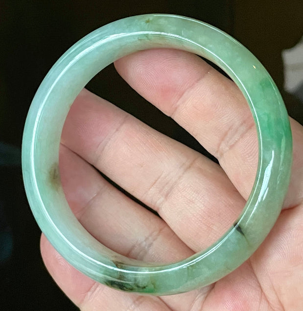 Hand holding a 58.6mm certified Grade A Burmese jadeite bangle in icy light bluish milky white with imperial & apple green and honey hues, item JB120