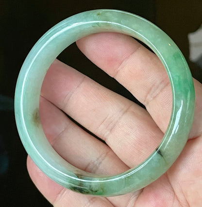 Hand holding a 58.6mm certified Grade A Burmese jadeite bangle in icy light bluish milky white with imperial & apple green and honey hues, item JB120