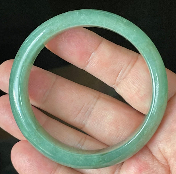 Hand holding a 58.4mm certified Grade A Burmese jadeite bangle in icy apple and emerald green with honey brown hues, item JB906