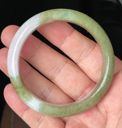 Hand holding a 58.4mm certified Grade A natural Burmese jadeite bangle in icy apple green and forest green with milky white hues, item JB078