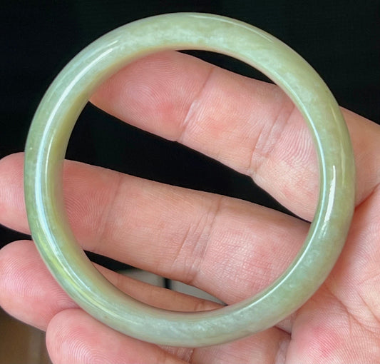 Hand holding a 55.2mm certified Grade A natural Burmese jadeite bangle in icy apple green, item JB507