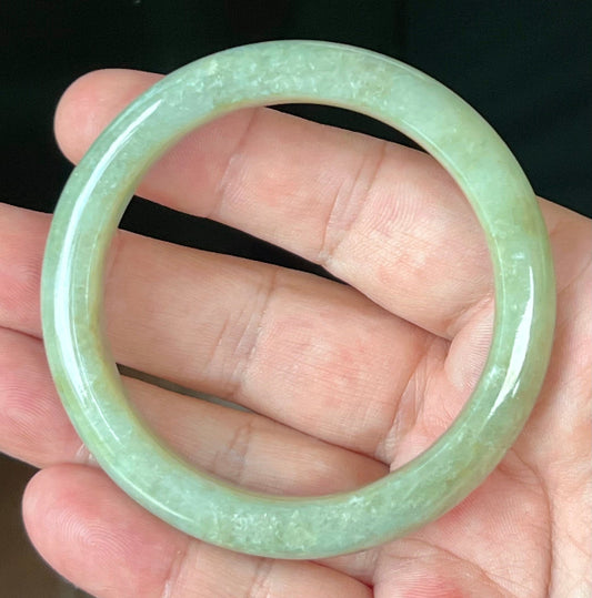 Hand holding a 55.5mm certified Grade A natural Burmese jadeite bangle in icy apple green, item JB558