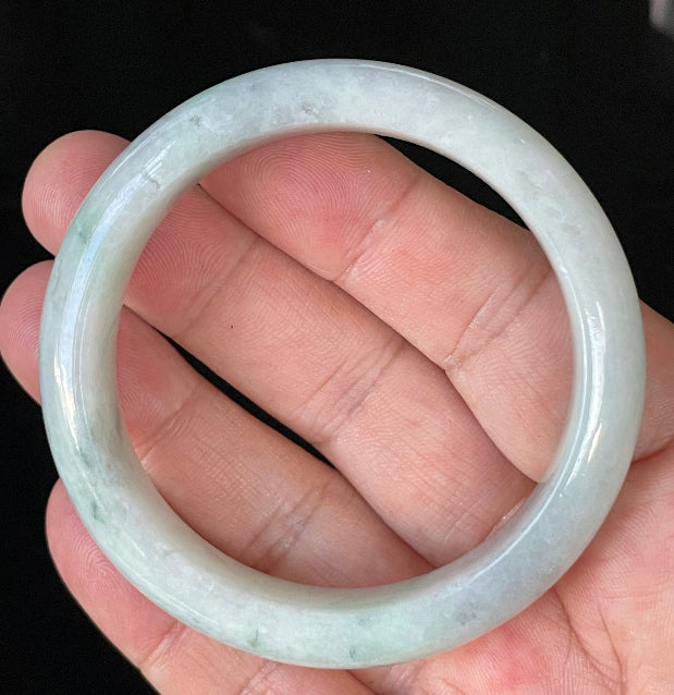 Hand holding a 55.2mm certified Grade A Burmese jadeite bangle in icy apple green and greyish milky white hues, item JB920