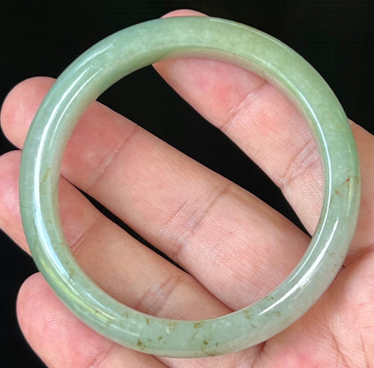 Hand holding a 55.2mm certified Grade A natural Burmese jadeite bangle in icy apple green with honey hues, item JB506