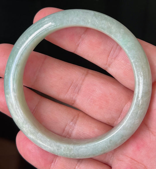 Hand holding a 55mm certified Grade A natural Burmese jadeite bangle in icy apple green with milky white tones, item JB518