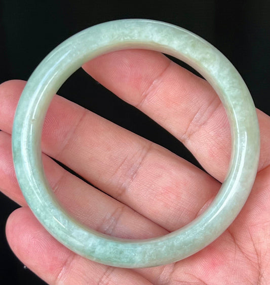 Hand holding a 56.8mm certified Grade A natural Burmese jadeite bangle in icy apple green and milky white, item JB537