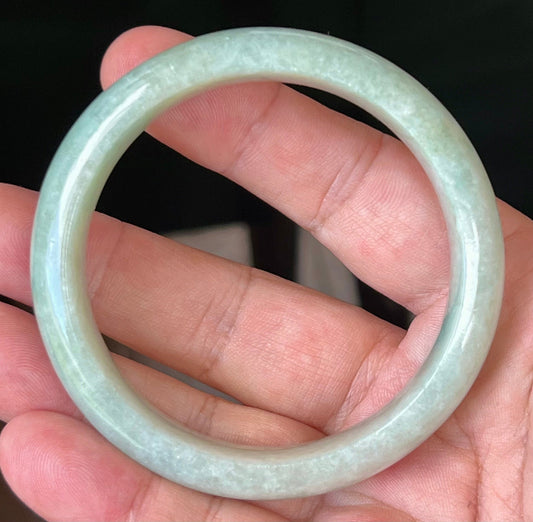 Hand holding a 58.3mm certified Grade A natural Burmese jadeite bangle in icy apple green and milky white hues, item JB548
