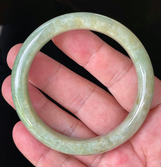 Hand holding a 58.2mm certified Grade A Burmese jadeite bangle in icy apple green, milky white, and honey brown hues, item JB830
