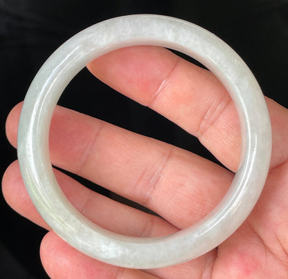 Hand holding a 56.7mm certified Grade A Burmese jadeite bangle in icy apple green and milky white with imperial green dots, item JB103