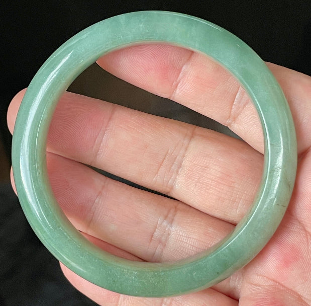 Hand holding a 58.5mm certified Grade A Burmese jadeite bangle in icy apple green and imperial green hues, item JB922
