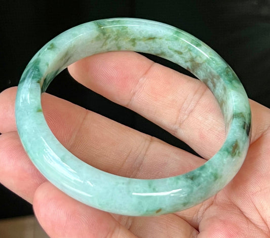 Hand holding a 57.7mm certified Grade A natural Burmese jadeite bangle in icy apple and imperial green with bluish milky white and black hues, item JB561