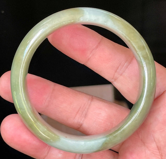 Hand holding a 57.5mm certified Grade A Burmese jadeite bangle in icy apple and moss green with bluish milky white hues, item JB032