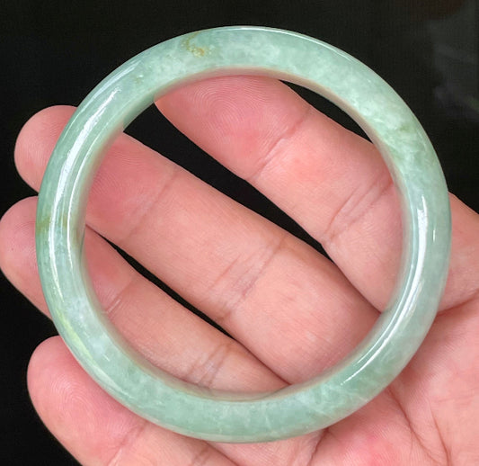 Hand holding a 55.5mm certified Grade A Burmese jadeite bangle in icy light bluish apple green with greyish milky white hues, item JB034