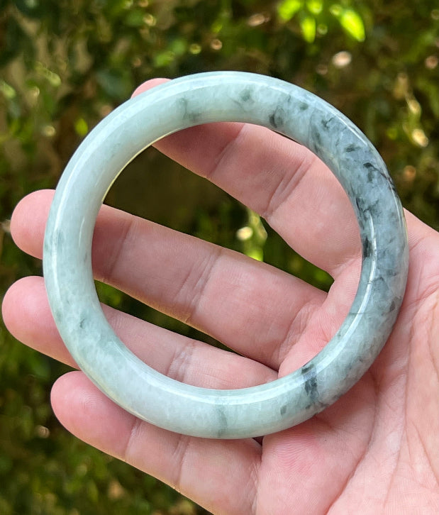 Close-up of moss green marbling and cloud-like formations on icy snow white jadeite bangle