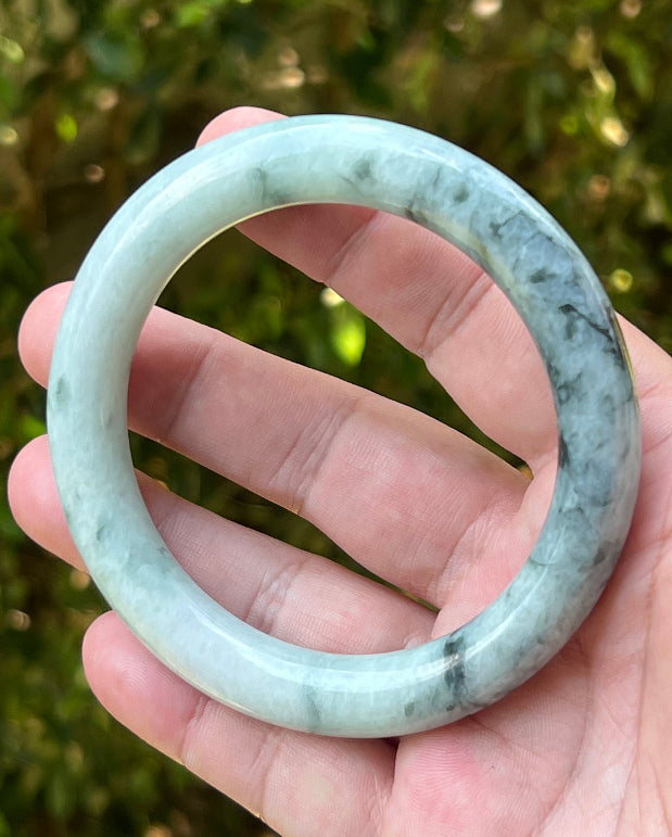 Close-up of moss green marbling and cloud-like formations on icy snow white jadeite bangle