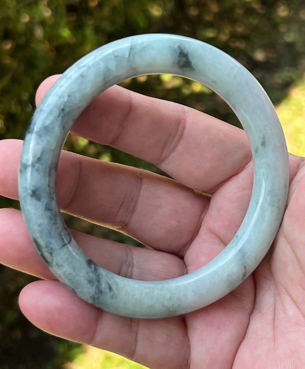 Close-up of moss green marbling and cloud-like formations on icy snow white jadeite bangle