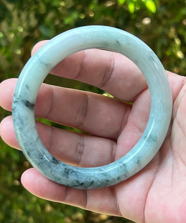 Close-up of moss green marbling and cloud-like formations on icy snow white jadeite bangle