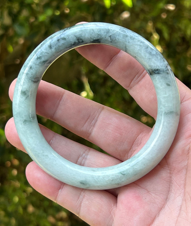 Close-up of moss green marbling and cloud-like formations on icy snow white jadeite bangle