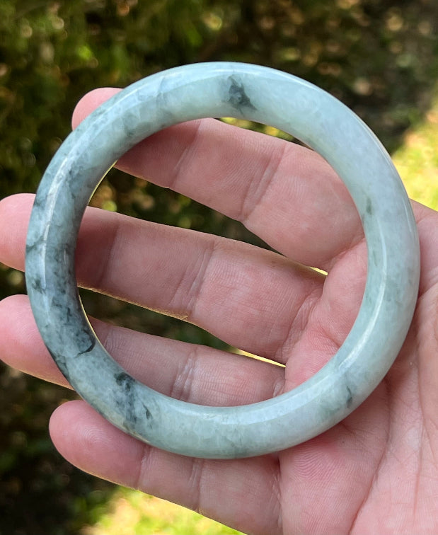 Close-up of moss green marbling and cloud-like formations on icy snow white jadeite bangle