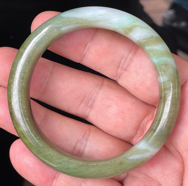 Hand holding a 54.7mm certified Grade A natural Burmese jadeite bangle in icy forest green with bluish and milky white hues, item JB353