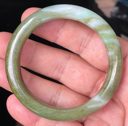 Hand holding a 54.7mm certified Grade A natural Burmese jadeite bangle in icy forest green with bluish and milky white hues, item JB353