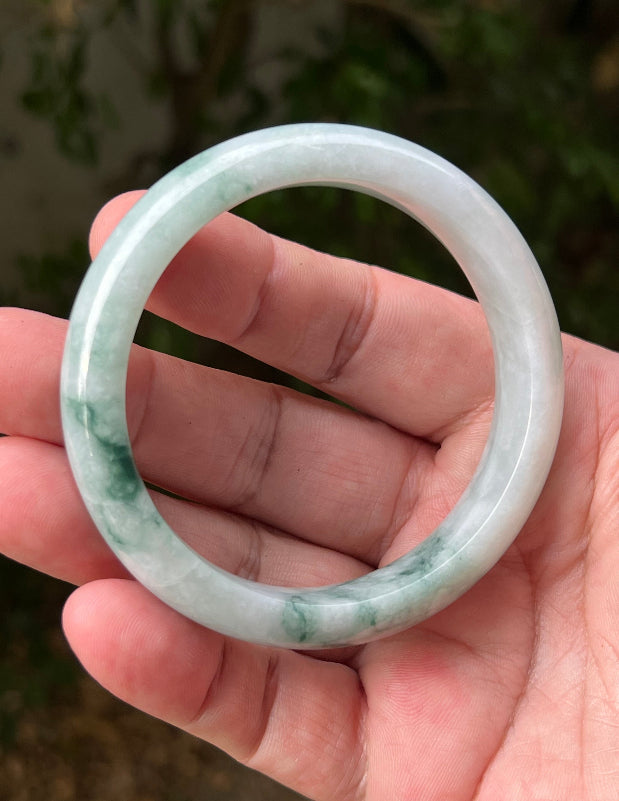 Hand holding a 58.5mm certified Grade A natural Burmese jadeite bangle in icy green and milky white, item JB1293