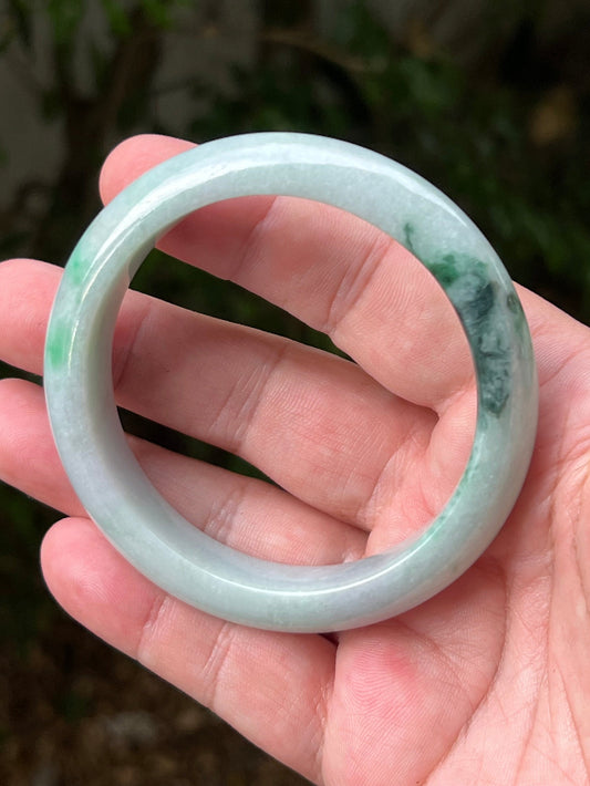 Hand holding a 60.5mm certified Grade A natural Burmese jadeite bangle in icy green and moss in snow, item JB1316