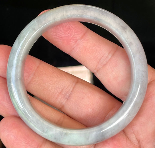 Hand holding a 57mm certified Grade A natural Burmese jadeite bangle in icy grey and milky white with honey hues, item JB358