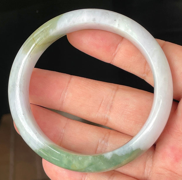 Hand holding a 58.6mm certified Grade A natural Burmese jadeite bangle in icy greyish milky white with apple and forest green hues, item JB095