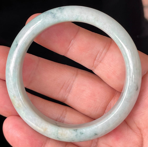 Hand holding a 53mm certified Grade A natural Burmese jadeite bangle in icy apple green with milky white and honey brown hues, item JB355