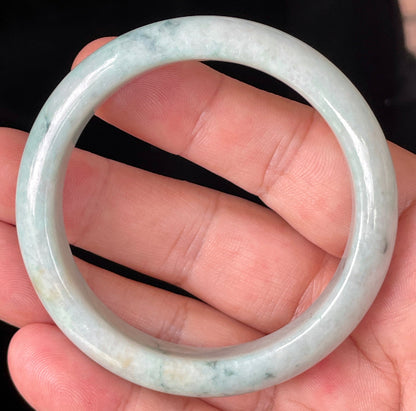 Hand holding a 53mm certified Grade A natural Burmese jadeite bangle in icy apple green with milky white and honey brown hues, item JB355