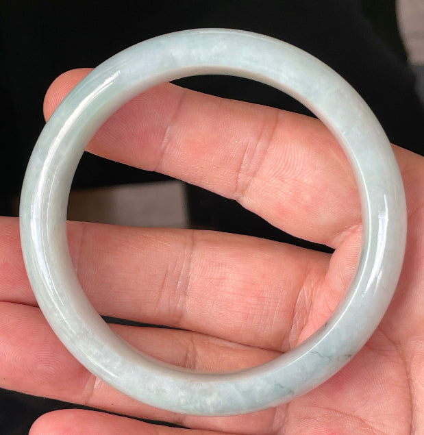 Hand holding a 58.8mm certified Grade A natural Burmese jadeite bangle in icy greyish milky white with light apple green and bluish hues, item JB231