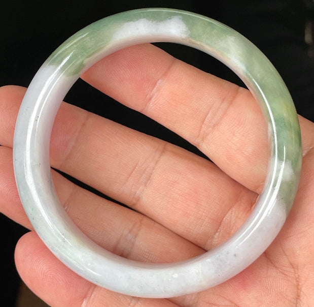 Hand holding a 58.5mm certified Grade A natural Burmese jadeite bangle in icy greyish milky white with apple and imperial green hues, item JB096
