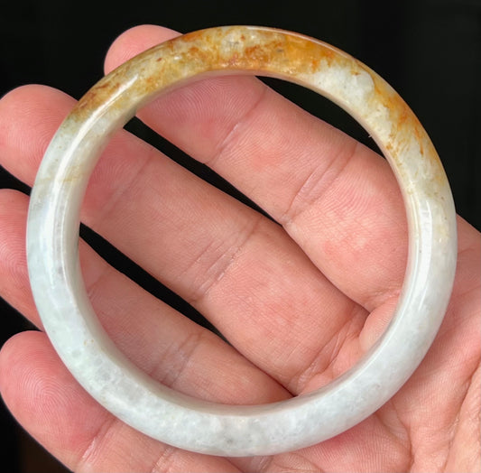 Hand holding a 58.4mm certified Grade A natural Burmese jadeite bangle in icy greyish milky white with orange red and honey hues, item JB531