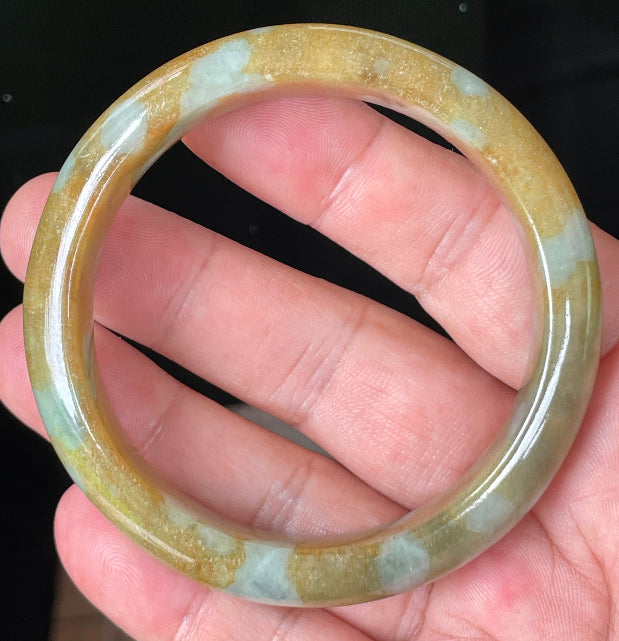 Hand holding a 58.4mm certified Grade A natural Burmese jadeite bangle in icy honey and brown with bluish milky white hues, item JB075