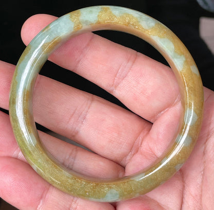 Hand holding a 58.6mm certified Grade A natural Burmese jadeite bangle in icy honey and brown with bluish and milky white hues, item JB094