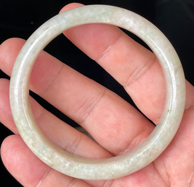 Hand holding a 59.8mm certified Grade A natural Burmese jadeite bangle in icy honey and milky white with light imperial green hues, item JB352